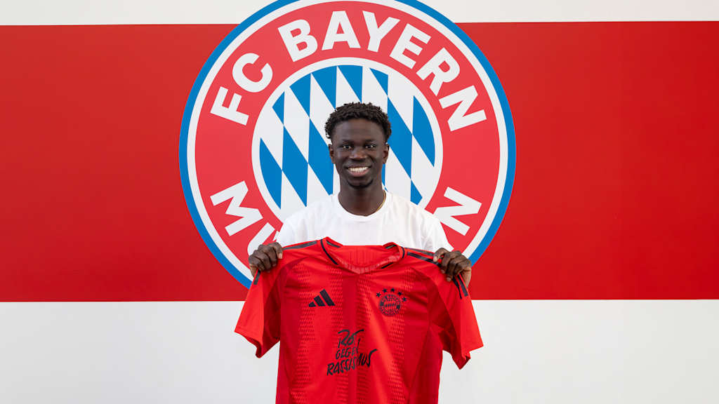 Bajung Darboe, FC Bayern II new signing, holds an FC Bayern home jersey in his hands.