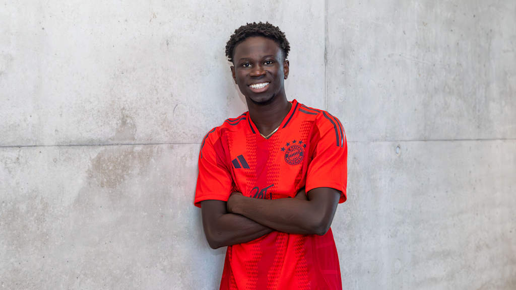FC Bayern II new signing Bajung Darboe in the FC Bayern home jersey in front of a grey wall.