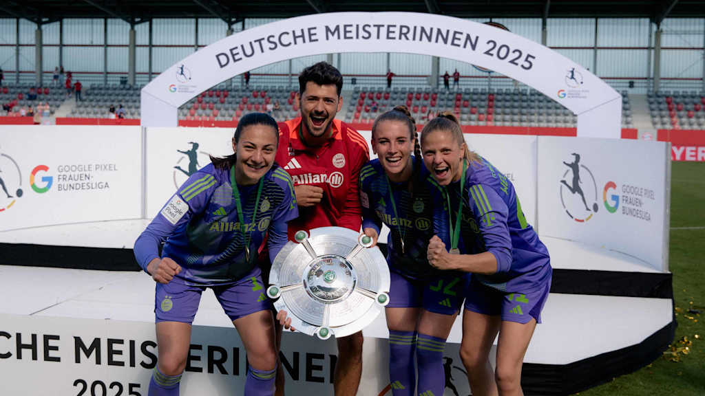 Goalkeepers Mala Grohs, Ena Mahmutovic and Anna Wellmann cheer into the camera alongside goalkeeping coach Michael Netolitzky and the 2025 Meisterschale.