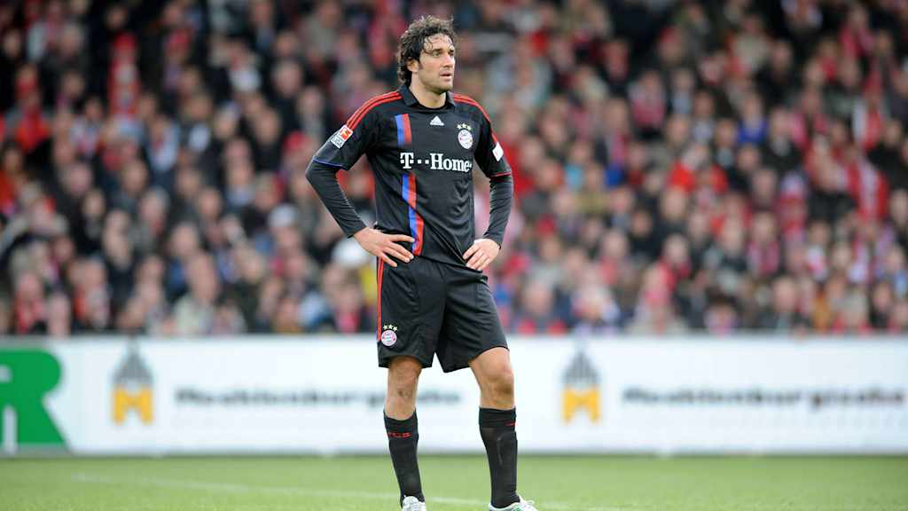Luca Toni está de pie sobre el césped en Cottbus con las manos en las caderas.