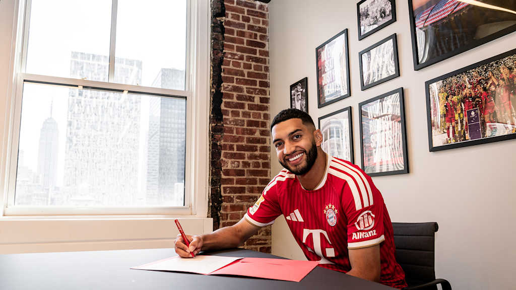 Ismael Saibari unterschreibt lächelnd im roten FC Bayern-Trikot ein Vertragspapier