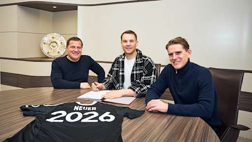 Max Eberl, Manuel Neuer und Christoph Freund sitzen an einem Tisch, Neuer unterschreibt einen Vertrag, auf dem Tisch liegt ein Trikot mit Neuer 2026