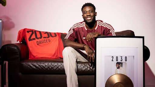 Alphonso Davies sitzt auf einer Couch und hält ein Albumcover mit 2030 im Arm