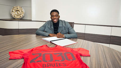 Alphonso Davies sitzt an einem Tisch und unterschreibt einen Vertrag
