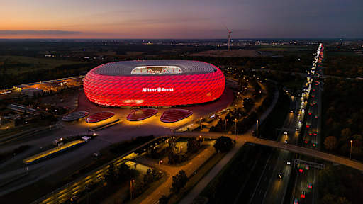 Allianz Arena strahlt in der Nacht in Rot, daneben die Autobahn