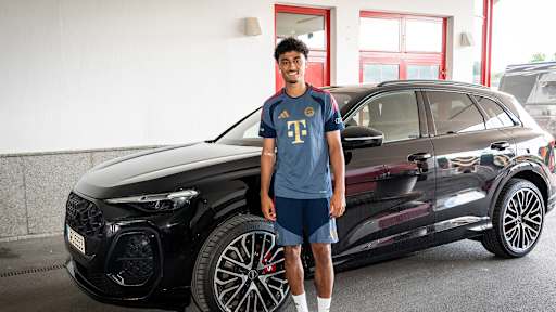Nathaniel Brown steht im FC Bayern-Trainingsshirt vor einem schwarzen Audi