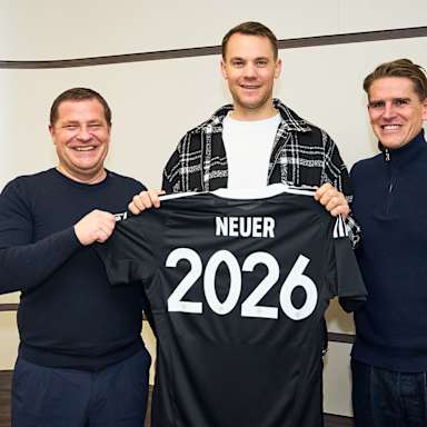 Max Eberl, Manuel Neuer und Christoph Freund stehen nebeneinander und halten ein Trikot mit Neuer 2026 hoch
