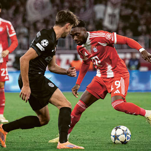 Vincent Kompany kniet im Training des FC Bayern auff dem Rasen und lacht.