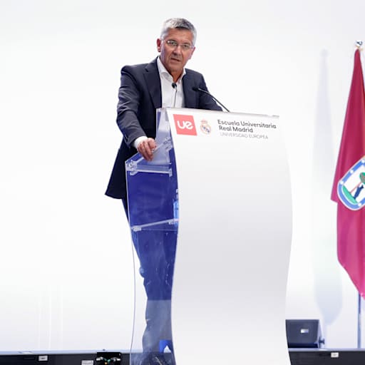 Herbert Hainer vor einem weißen Pult bei einer Rede vor Universitätsabsolventen im Bernabeu