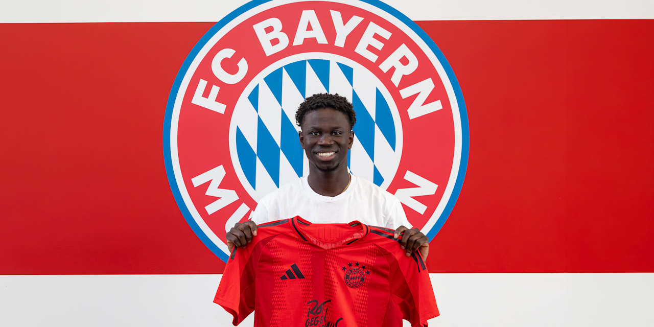 Bajung Darboe, FC Bayern II new signing, holds an FC Bayern home jersey in his hands.