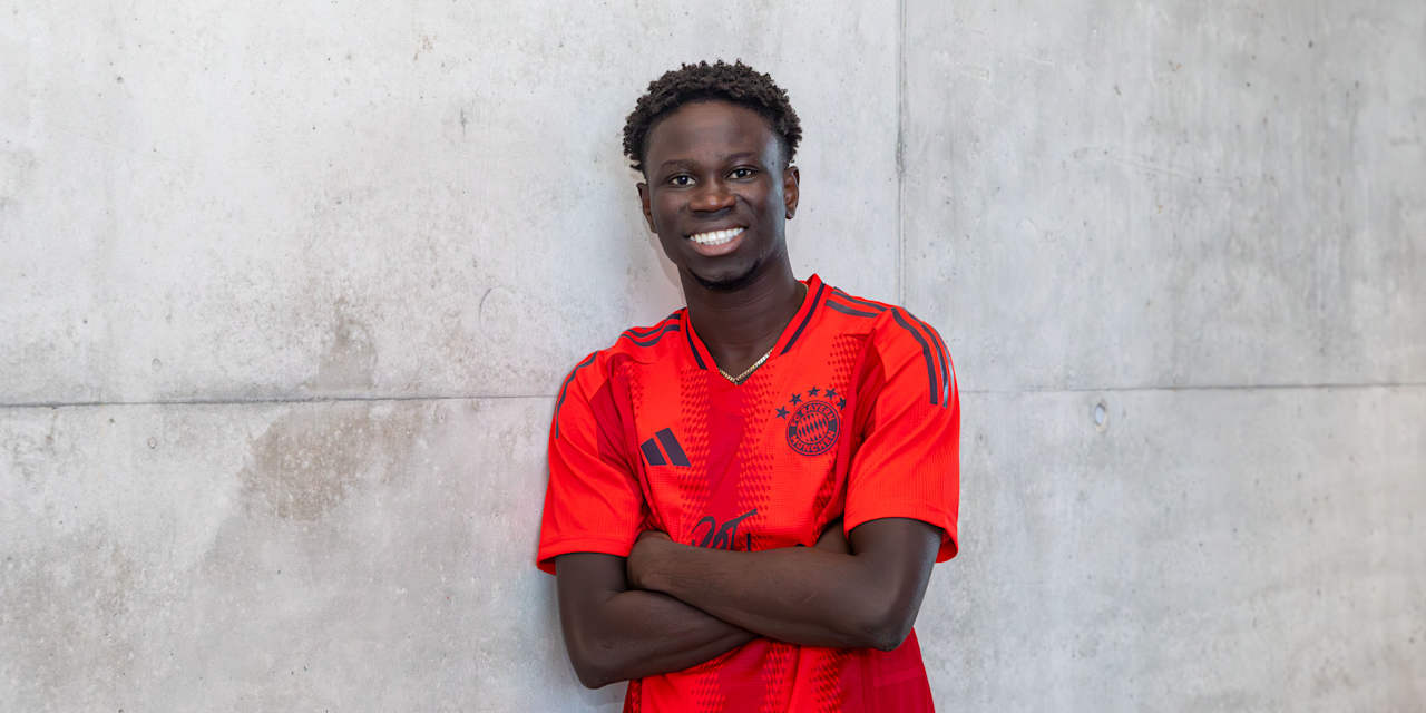 FC Bayern II new signing Bajung Darboe in the FC Bayern home jersey in front of a grey wall.