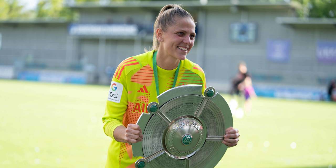 A smiling Anna Wellmann in her yellow goalkeeper jersey holding the Meisterschale and smiling.