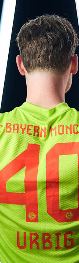 Jonas Urbig steht mit dem Rücken zur Kamera und zeigt auf seinen Rücken, dem Trikot mit der Nummer 40