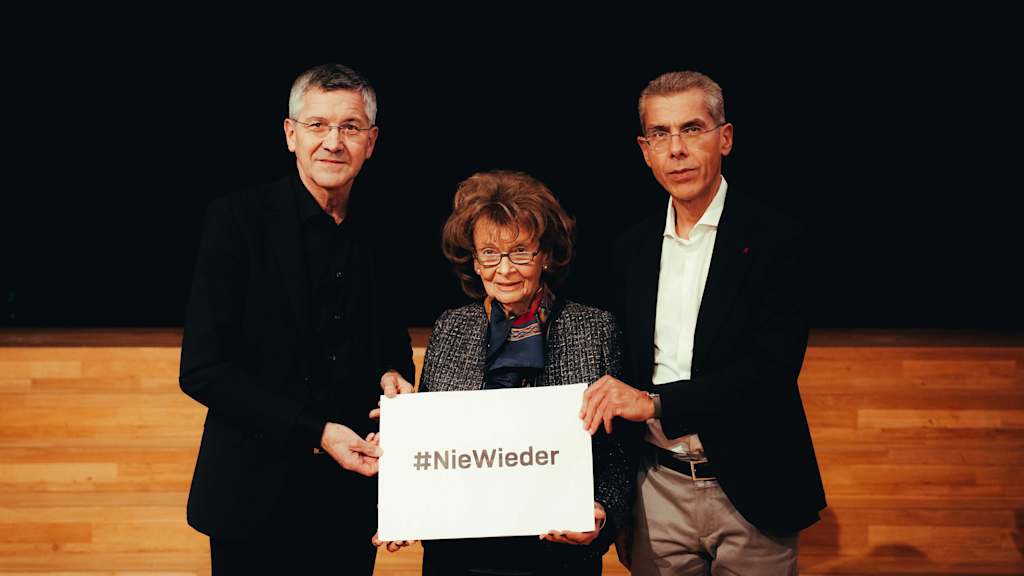 Zum Holocaust-Gedenktag halten Herbert Hainer, Charlotte Knobloch und Michael Diederich die Aufschrift #Niewieder hoch