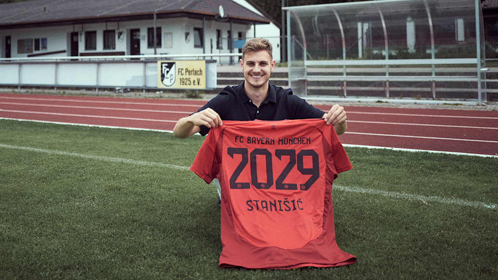Josip Stanisic hält auf dem Platz seines Jugendvereins FC Perlach ein Trikot des FC Bayern hoch.