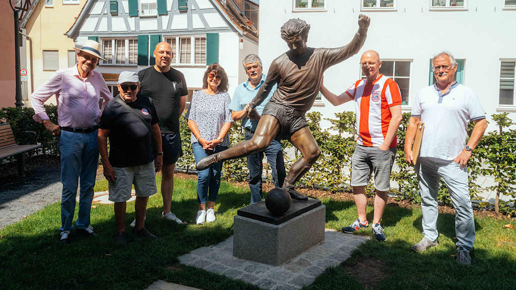 FC Bayern-Fans stehen neben der Statue von Gerd Müller in Nördlingen.