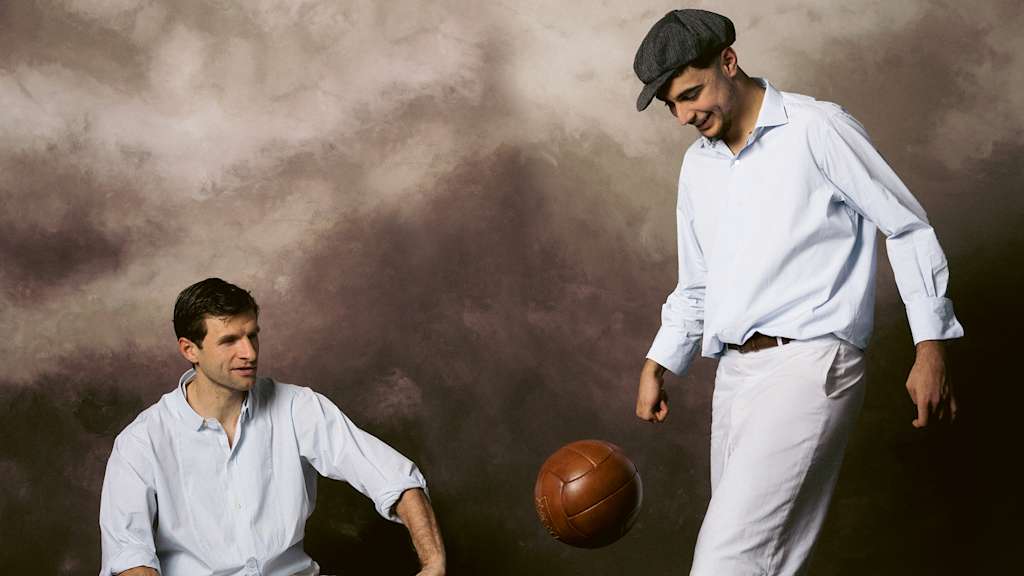 Aleksandar Pavlovic jongliert mit einem alten Lederball, Thomas Müller sitzt auf einer Holzbank