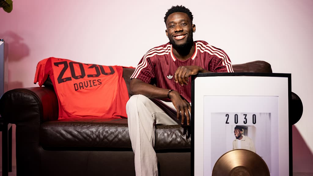 Alphonso Davies sitzt auf einer Couch und hält ein Albumcover mit 2030 im Arm