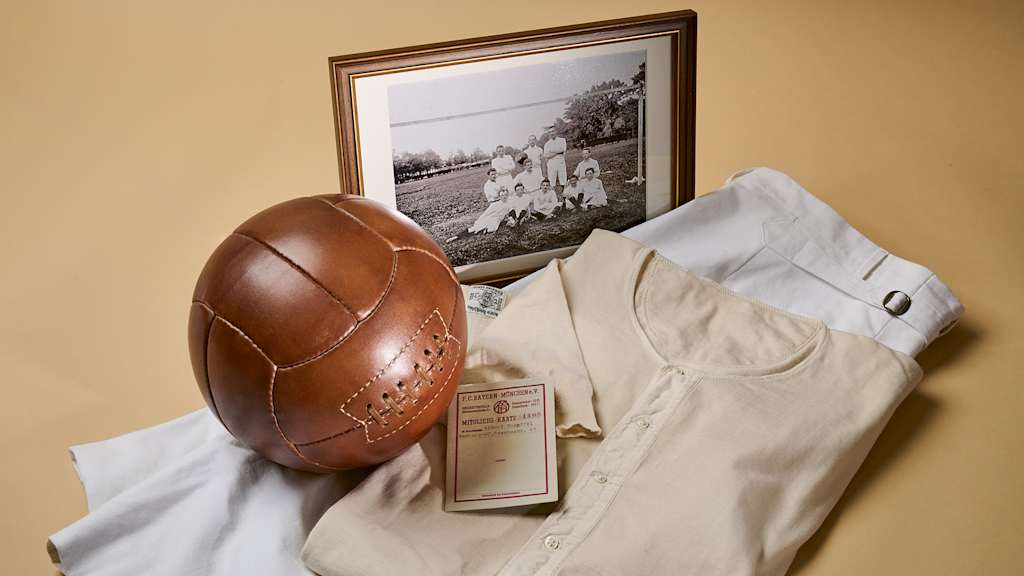 Das historische Trikot des FC Bayern, eine Hose, ein Ball und ein Foto liegen auf dem Boden