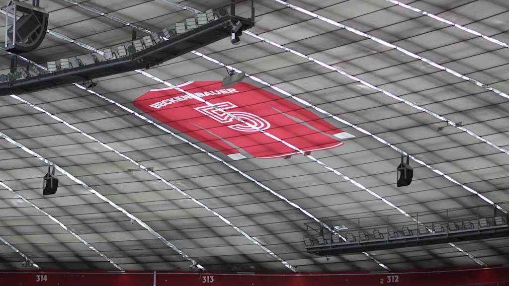 Ein rotes Trikot von Franz Beckenbauer mit einer weißen 5 hängt unter dem Dach der Allianz Arena