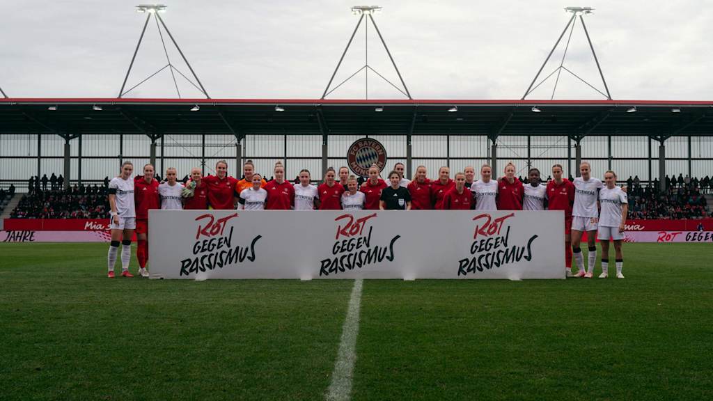 Die Spielerinnen des FC Bayern und von Bayer Leverkusen stehen gemeinsam vor einem Banner mit der Aufschrift Rot gegen Rassismus.