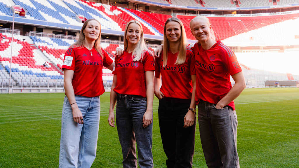 FC Bayern Women's Sydney Lohmann, Giulia Gwinn, Klara Bühl and Pernille Harder posing in FCB jerseys on the pitch in the Allianz Arena.