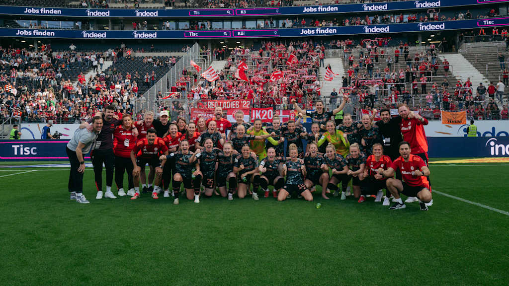 Die jubelnde Mannschaft in einem Gruppenfoto vor dem FC Bayern Fanblock.