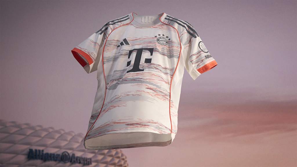 La nueva segunda equipación del FC Bayern para la temporada 2025/26 en blanco, gris y coral brillante ondea frente al Allianz Arena.