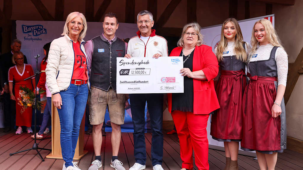 Präsident Herbert Hainer zeigt in einer Gruppe Personen einen Scheck in die Kamera beim Fanfest im Bayern Park