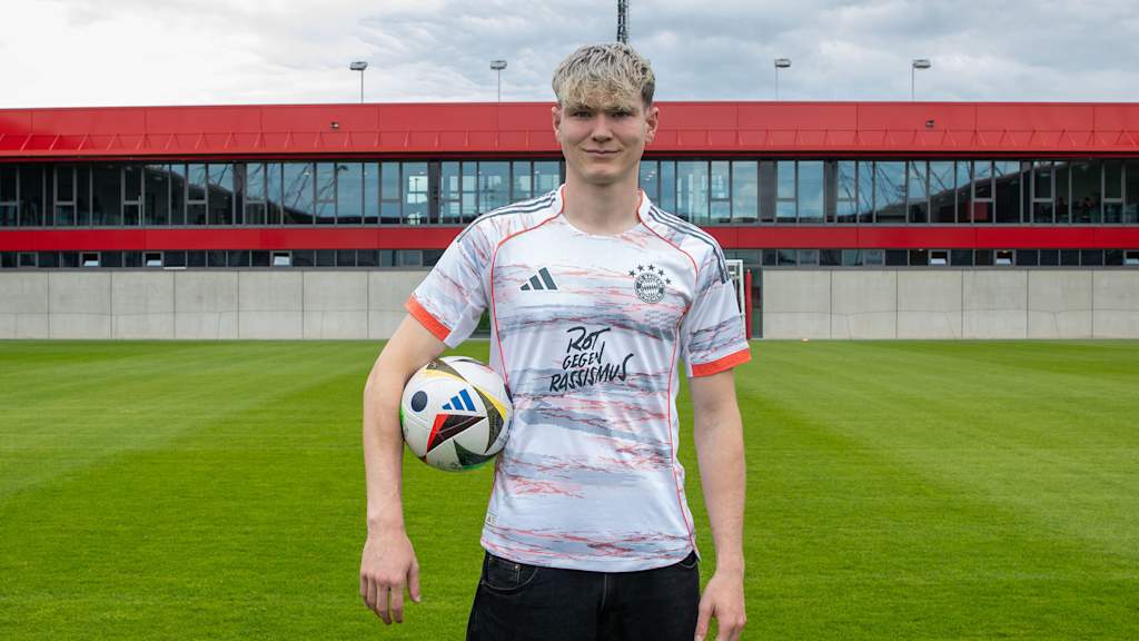Richard Meier steht auf dem Platz in der Spielstätte am FC Bayern Campus mit einem Ball unter der rechten Hand.
