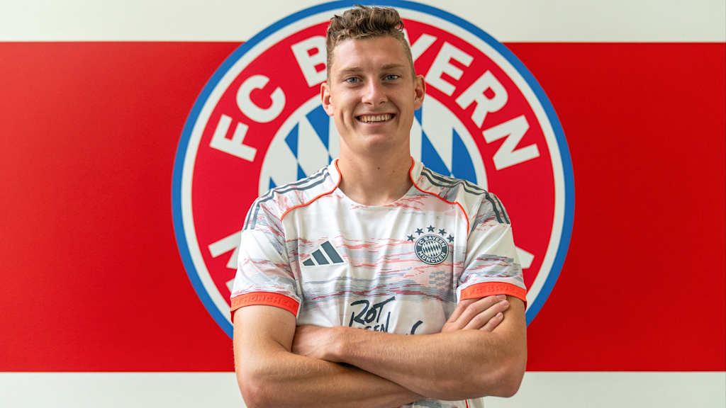 David Heindl und posiert im Trikot vor dem FC Bayern-Wappen am FC Bayern Campus.