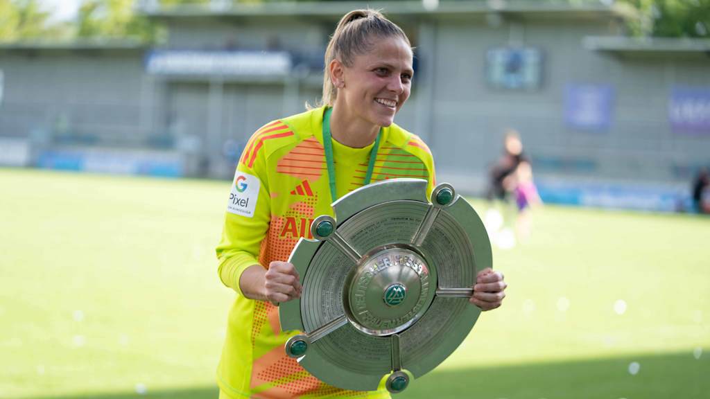 A smiling Anna Wellmann in her yellow goalkeeper jersey holding the Meisterschale and smiling.