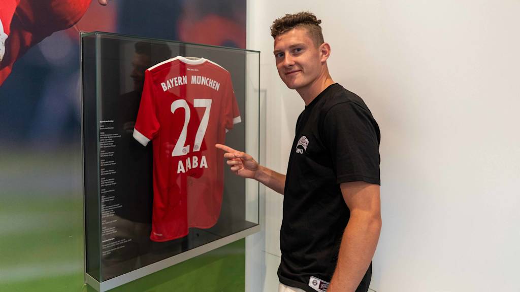 David Heindl zeigt auf ein David Alaba Trikot im Eingang des FC Bayern Campus
