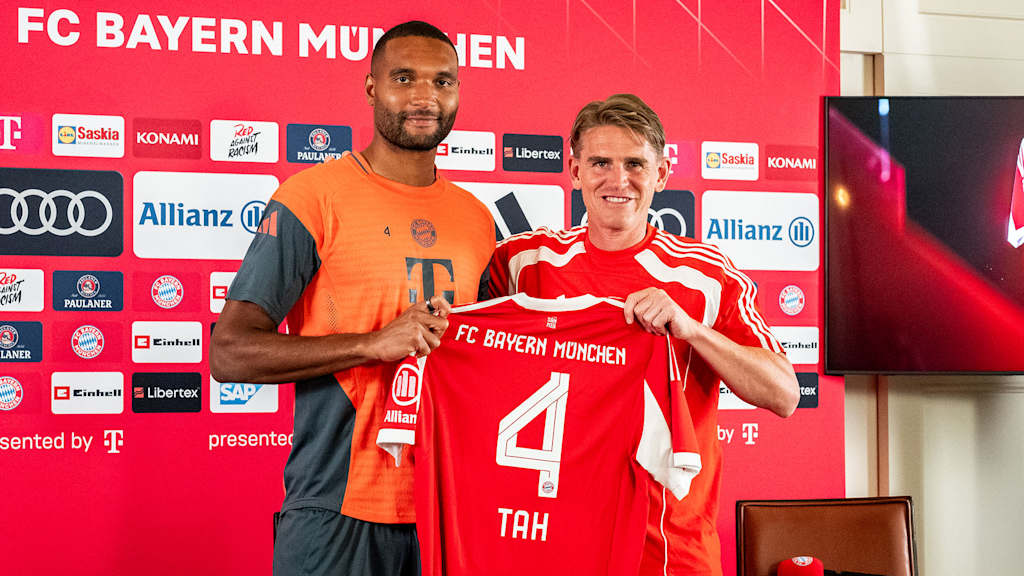 Jonathan Tah und Christoph Freund halten ein FCB-Trikot mit der Rückennummer 4 hoch