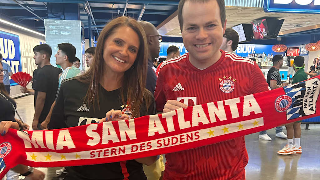 Heather Cooke and Chris Clute wearing Bayern jerseys and a Bayern scarf with the words ‘Mia san Atlanta’ written on it.