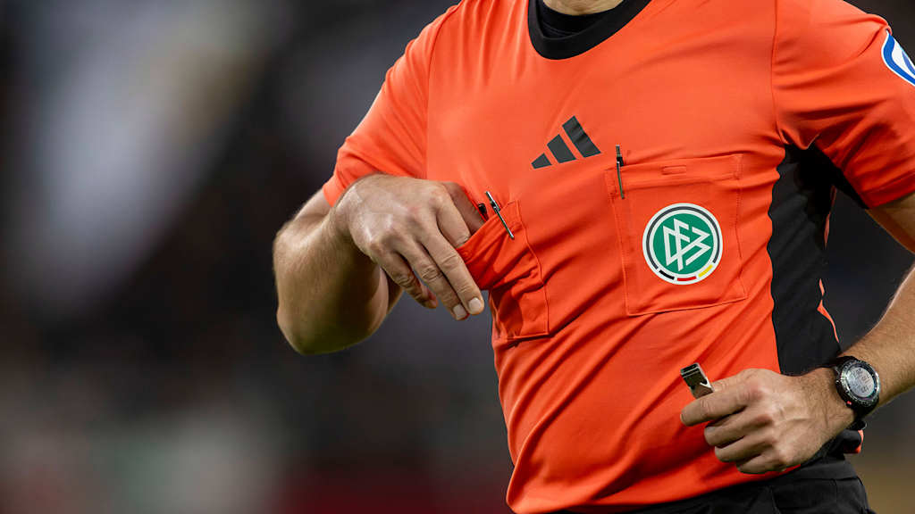 Ein Bundesliga-Schiedsrichter zieht die gelbe Karte aus der Brusttasche.