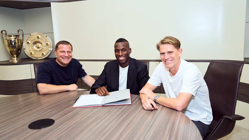 Max Eberl, Nicolas Jackson, Christoph Freund sitzen an einem Tisch, Jackson unterschreibt einen Vertrag