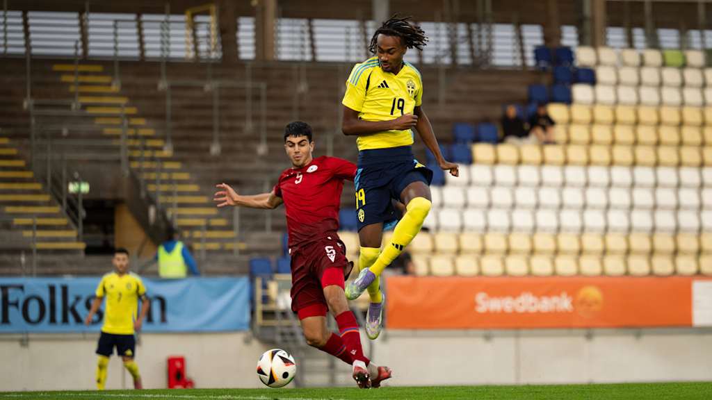 Jonah Kusi-Asare, im Trikot von Schweden, springt über das Bein seines Gegenspielers nachdem er den Ball gespielt hat.