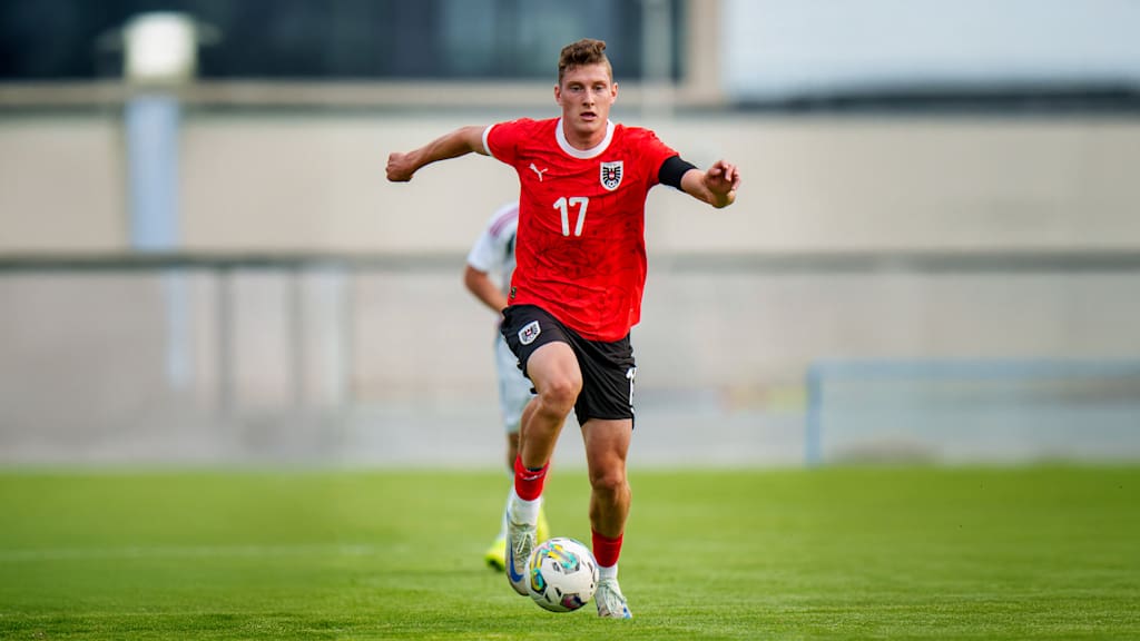 David Heindl schaut im Trikot der Österreichischen Nationalmannschaft konzentriert während er den Ball am Fuß hat.