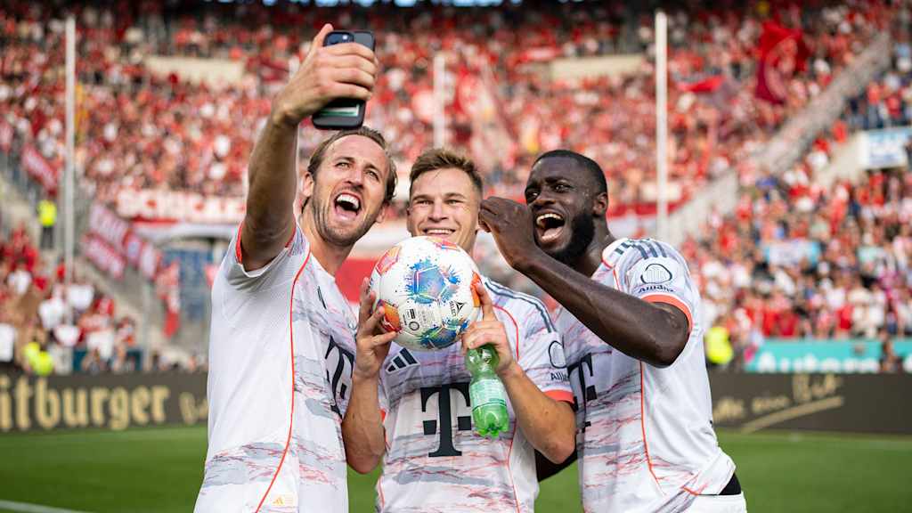 Harry Kane, Joshua Kimmich and Dayot Upamecano take a selfie in front of the visitors' block in Sinsheim in their white jerseys.