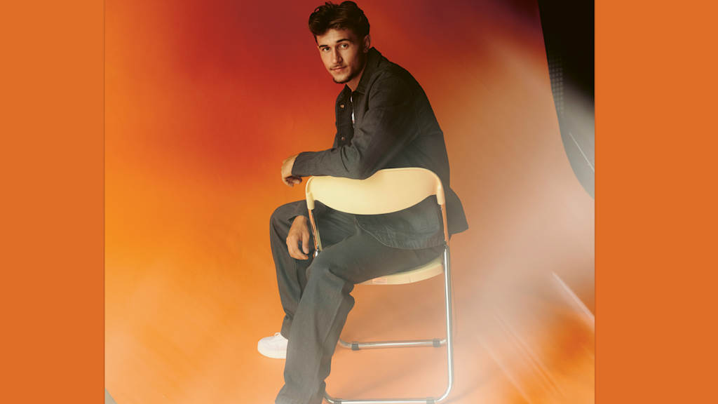 Tom Bischof sitting casually on a chair in front of an orange canvas