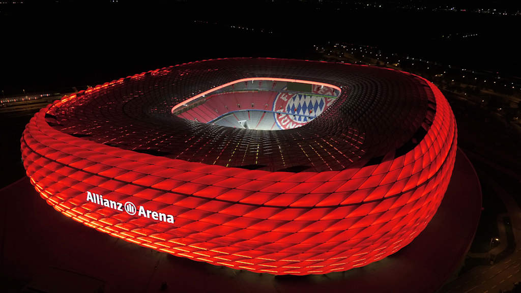 The Allianz Arena lit up in red at night from a birds-eye view.