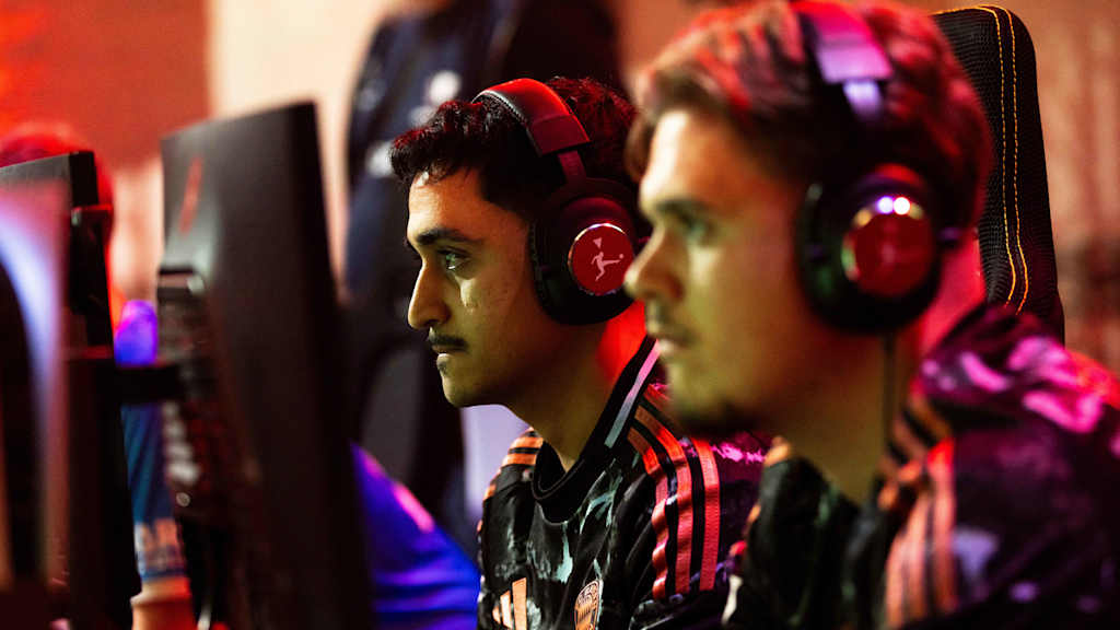 Dos hombres están sentados frente al televisor con auriculares y juegan a videojuegos.