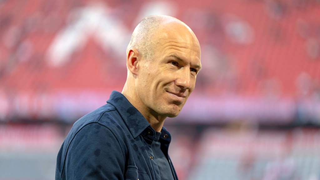 Arjen Robben grins into the camera in a blue shirt.