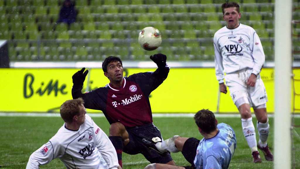 Giovane Elber blickt beim  Pokalspiel gegen Köln am Boden hockend auf dem Ball, umringt von liegenden Kölnern