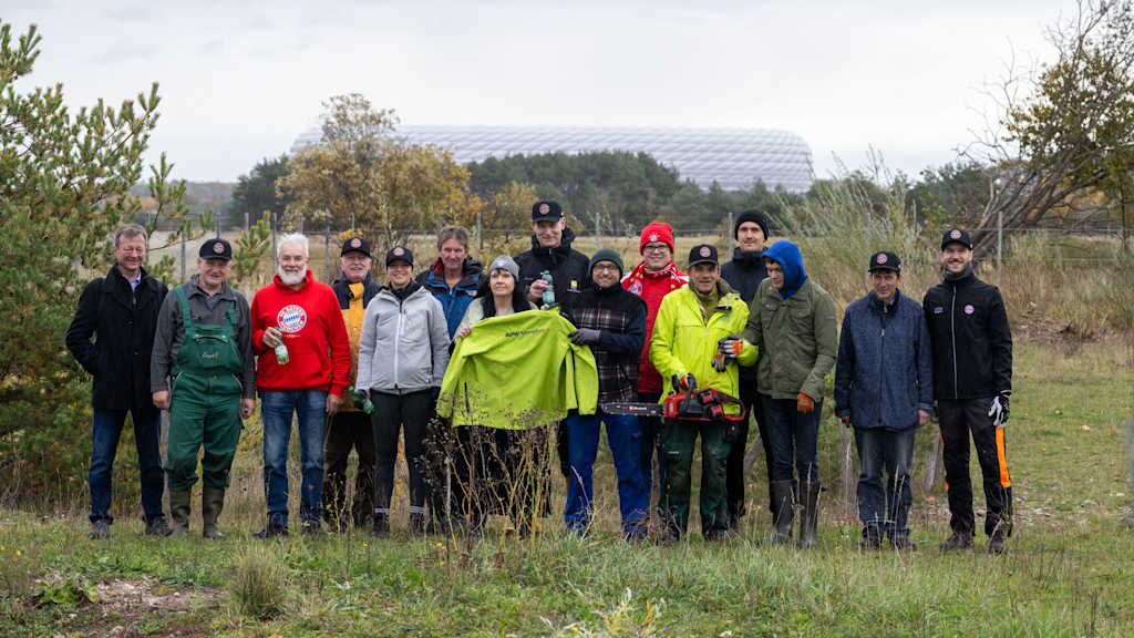 A group of helpers stands in the countryside, the outline of the Allianz Arena can be seen in the background