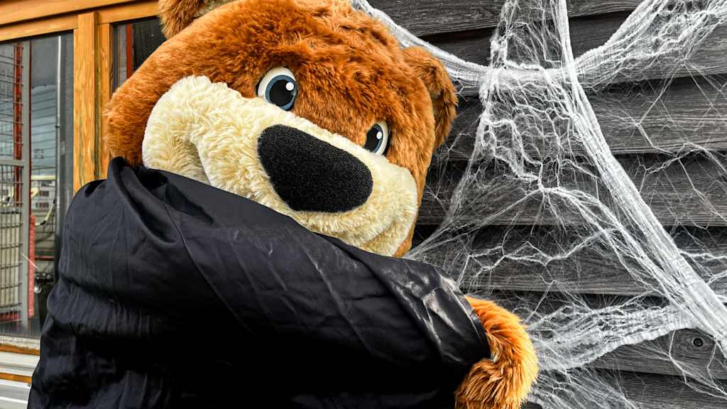 Berni steht mit einem schwarzen Umhang vor einer Hauswand mit Spinnenweben.