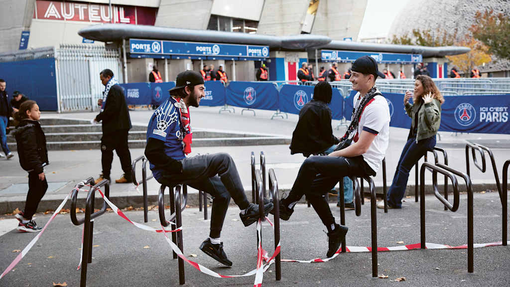 Two fans sit in front of the stadium in Paris with club merchandise