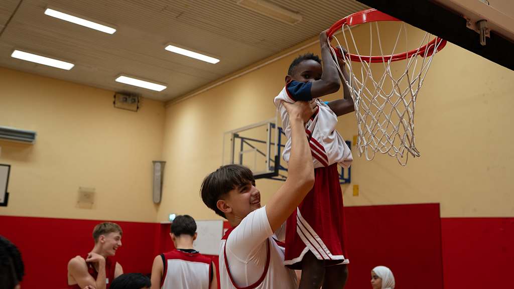 Ein kleiner Junge wird von Mitspieler zum Korb gehoben