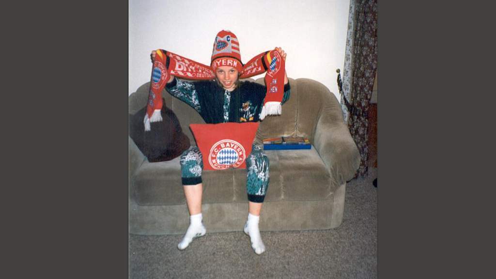 Ein junger Bayern-Fan hätt auf dem Sofa den Bayern-Schal in die Luft